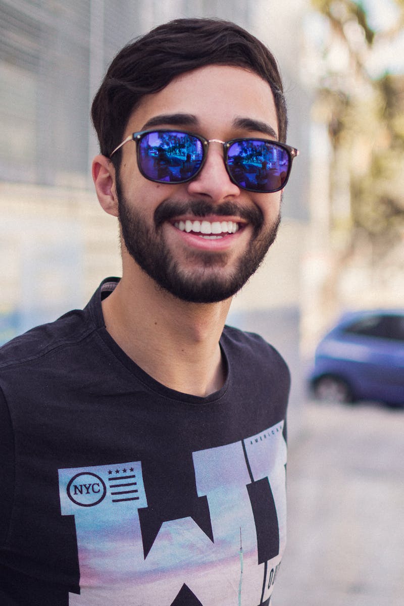 Portrait of a smiling man wearing sunglasses outdoors, showcasing modern fashion and style.